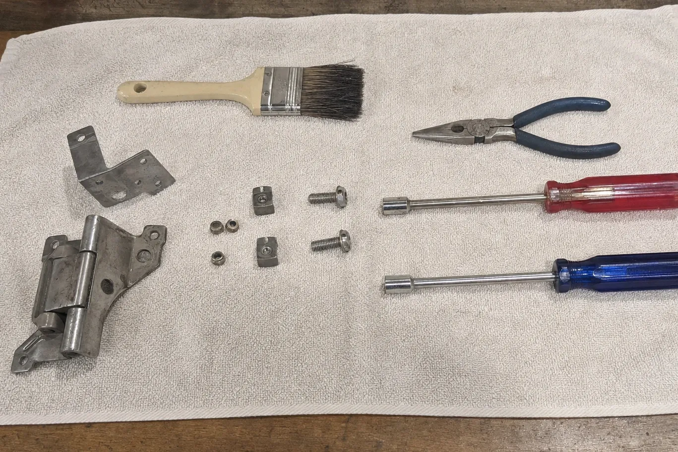 Oven door hinge assembly laid out on a towel with a bracket, spacer blocks, bolts, pliers and nut drivers