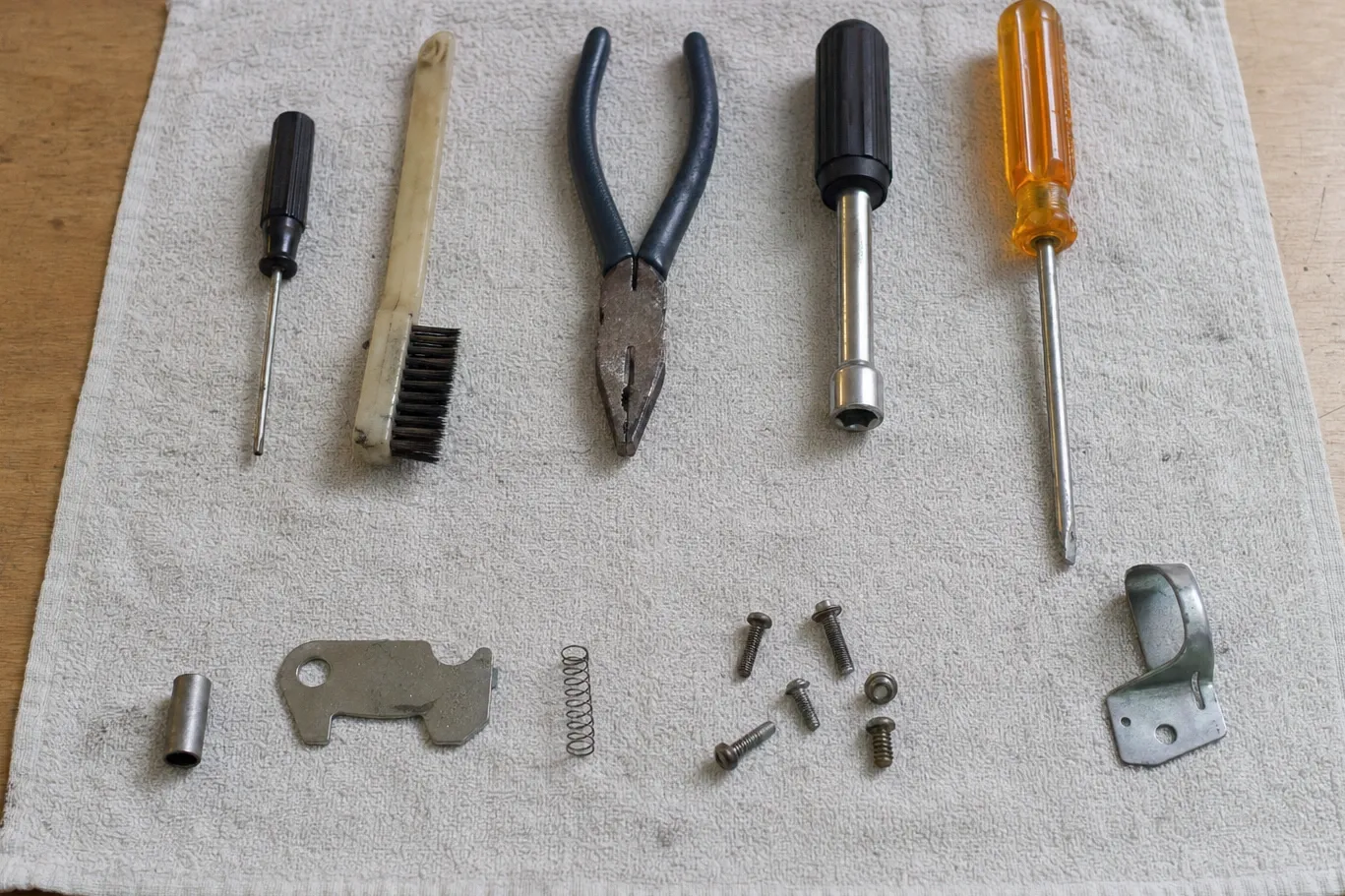 Wire brush, pliers, drivers, a latch plate, a coil spring and assorted screws laid out on a folded towel